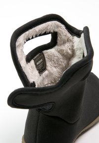 Botas de goma negras con una superficie texturizada, forro de piel de pato gris y una cinta de tirón para facilitar el uso. Etiqueta interior visible.