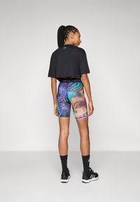 Černé zkrácené tričko s krátkými rukávy; barevné vzorované těsné šortky s grafikou; černé sportovní ponožky; černá obuv s bílými akcenty.