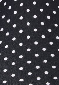 Tessuto nero con pois bianchi, ogni pois è uniformemente distanziato, creando un motivo uniforme. Texture liscia con una leggera lucentezza.
