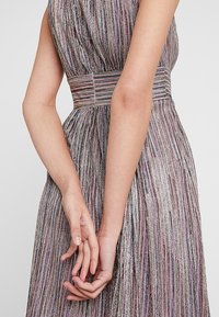 Robe scintillante à rayures multiples en rose, argent et lavande. Présente une taille cintrée et une jupe fluide avec un tissu texturé.
