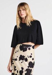 Maglione nero corto con maniche corte abbinato a una gonna beige con un motivo astratto nero. Texture lavorata a maglia e vestibilità comoda.