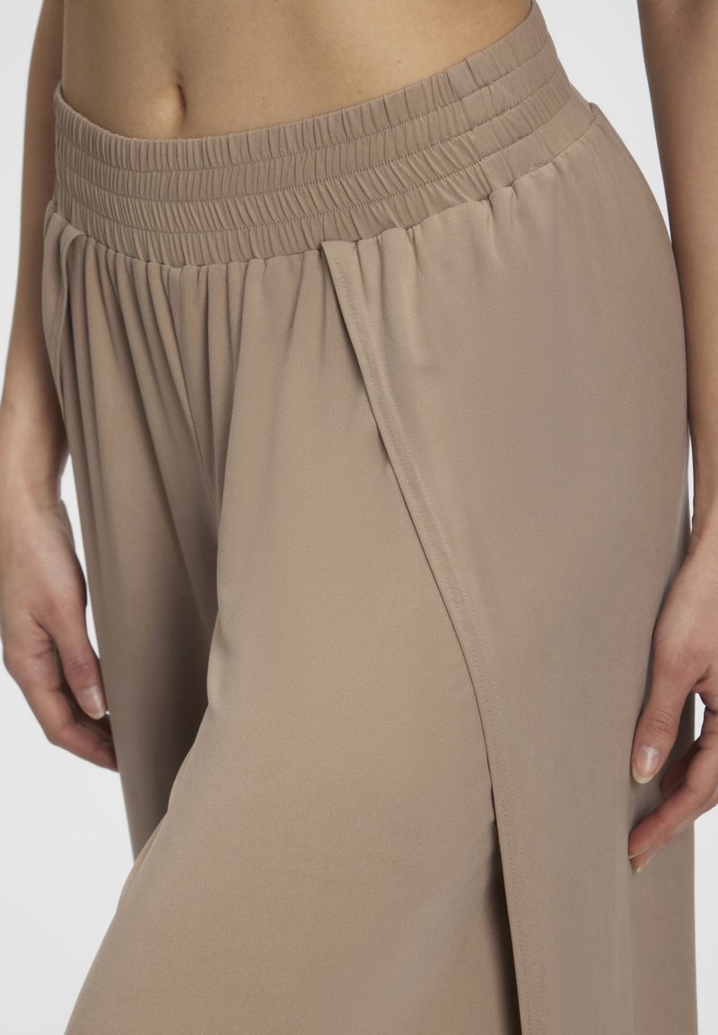 Beige trousers made of lightweight fabric with an elastic waistband, featuring side slits and a relaxed fit for ease of movement.