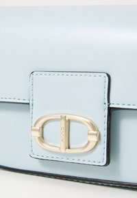 Bolso de piel de color azul claro con un broche dorado, ribetes negros y costuras detalladas. Textura suave con una forma estructurada.
