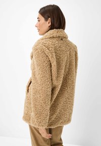 Tan faux fur jas met een zachte, gestructureerde afwerking, voorzien van een sjawl-kraag en zijzakken. Eenvoudige, ontspannen silhouet.