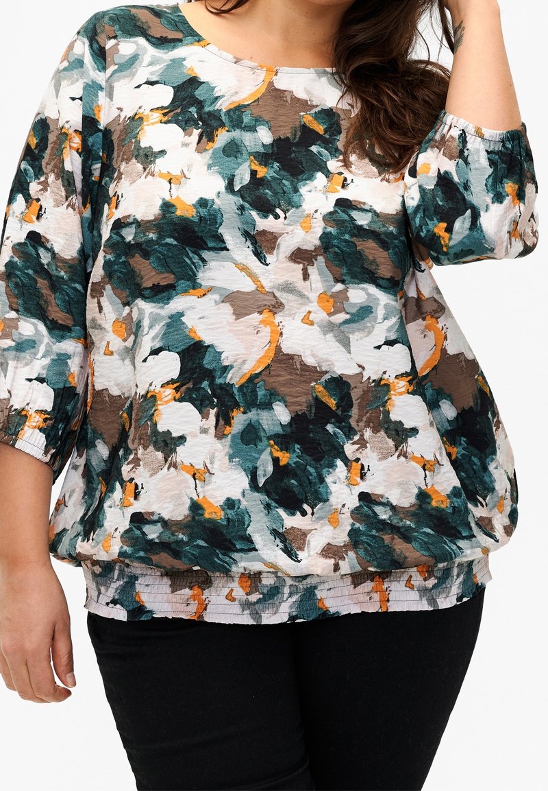 Top de estampado floral en verde, marrón y naranja sobre un fondo claro; cuenta con mangas tres cuartos y un corte relajado con dobladillo fruncido.
