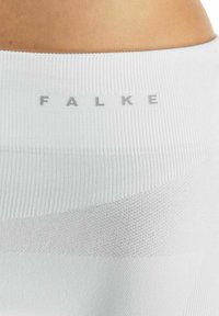 Witte geribde legging met een gladde textuur en een contrasterende band. "FALKE" logo in lichtgrijs op de tailleband.