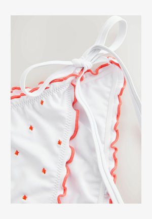 Valkoisen bikinin yläosa, jossa on korallinväriset aaltoilevat reunat ja pieniä oransseja koristeita, takana solmittava kiinnitys. Pehmeä pinta.