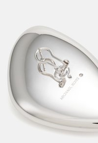 Sølvmetall øredobber med en buet, polert overflate, som har en dekorativ krok og gravert "MICHAEL KORS" på bunnen.
