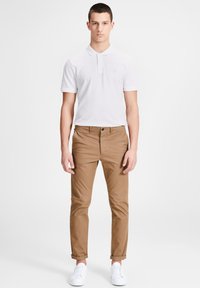 Polo blanc avec un col associé à un pantalon chino beige. Tissu léger et doux ; le pantalon a une coupe slim, des poignets retournés et est longueur cheville. Baskets blanches.
