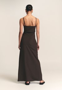 Braunes ärmelloses Maxikleid mit dünnen Trägern, tailliertem Oberteil und fließendem Rock. Glatte Textur, knöchellang, minimalistisches Design.