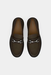 Hnedé topánky na nazutie z mäkkého zamatového materiálu, zaoblenou špičkou, dekoratívnymi kovovými prvkami a pohodlnou hnedou stielkou.