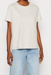 T-shirt in cotone beige chiaro con scollo rotondo, maniche corte e logo Calvin Klein ricamato sul petto. Vestibilità rilassata.