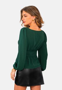 Top verde de manga larga con cintura fruncida y corte holgado, combinado con una falda negra de cuero sintético. Textura suave y diseño clásico.