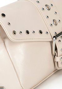 Borsa a tracolla in eco-pelle beige con borchie argentate e accessori metallici, dotata di chiusura a patta e finitura texture.