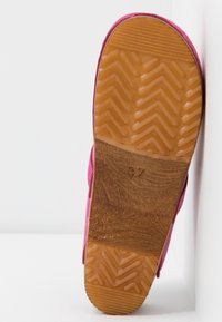 Semelle d'une chaussure rose avec une section centrale brune texturée et une bande de roulement en caoutchouc orange présentant des motifs en chevrons et rayures.