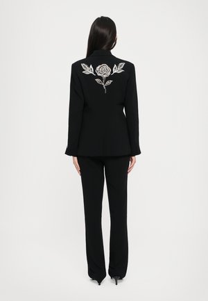 Black tailored suit featuring a fitted blazer with a rose and leaf embroidery in silver on the back, paired with straight-leg trousers.
