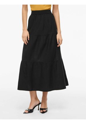 Femme portant une jupe midi noire évasée à taille haute associée à des mules à talons noires à bouts ouverts et un haut moutarde raccourci au-dessus de la taille.