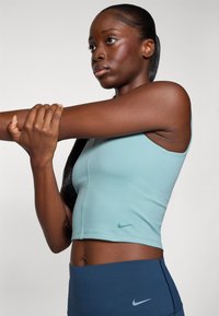 Light blue cropped sports top with a fitted design and green Nike logo, paired with navy blue high-waisted leggings. Smooth fabric texture.