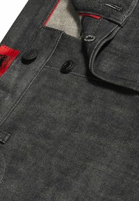 Harmaa denim, jossa on himmeä rakenne. Varusteena mustat metallinapit ja punainen logo-tunnus. Erottauduvat saumat ja näkyvä vuori.