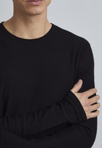 Zwarte longsleeve shirt gemaakt van een zachte, gestructureerde stof. Het heeft een ronde hals en aansluitende mouwen met verlengde manchetten.