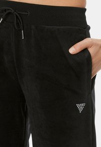 Pantaloni jogger neri in velluto con vita regolabile tramite coulisse, tasche laterali e un accento a triangolo con strass nella parte inferiore della gamba. Tessuto morbido.