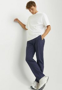 T-shirt bianco a maniche corte, pantaloni blu navy con tasche e sneakers grigio chiaro. Il tessuto ha una texture liscia, con una vestibilità comoda.