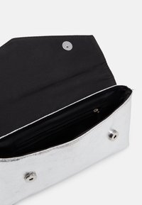 Silver metallic clutch bag with a sleek design, featuring a black interior, snap closure, and interior zip pocket. Smooth texture.