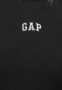 Tissu côtelé noir avec des lettres blanches brodées "GAP" centrées sur la zone de la poitrine.