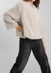 Maglione fuzzy beige chiaro con una finitura testurizzata e maniche ampie, abbinato a jeans scuri a vestibilità rilassata. Scollo rotondo semplice.