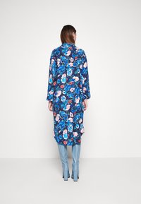 Abito floreale lungo di colore blu scuro con fiori rosa e blu, caratterizzato da maniche lunghe e un orlo leggermente curvo. Abbinato a stivali blu.