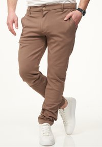 Brown tapered pants made of soft fabric with front pockets and a button closure, paired with white sneakers. Smooth texture.