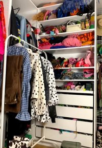 Kast met witte planken met gevouwen kleding, tassen en accessoires; kledingrek met jassen en broeken vooraan.