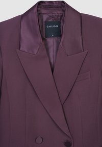 Blazer doppiopetto in un profondo viola, con revers in satin, spalle strutturate, taschino sul petto e una finitura liscia e sartoriale.