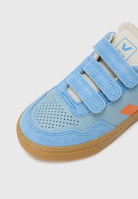 Pantof sport albastru din piele întoarsă și piele netedă, cu trei benzi velcro, vârf perforat și talpă din cauciuc tip gumă. Accesoriu portocaliu pe lateral.