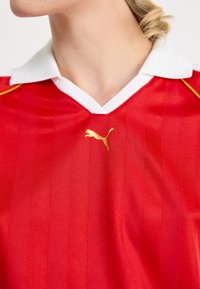 Red sports jersey with vertical stripes, white collar, and gold Puma logo. Made of smooth, lightweight fabric designed for athletic wear.