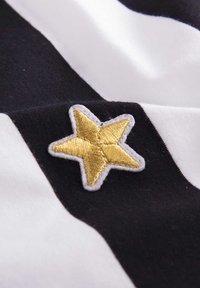 Zwart-wit gestreepte stof met een gouden geborduurde sterpatch, omrand met witte stiksels, die een zachte textuur en levendig contrast toont.