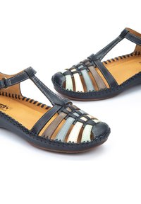Sandalias con tiras que presentan una combinación de bandas en azul oscuro, marrón y tonos pastel, con un borde cosido y una plantilla de madera para mayor detalle.