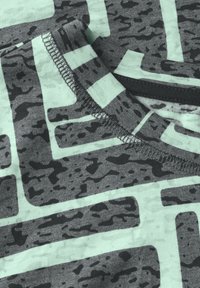 Šedá a mátově zelená látka s abstraktními vzory. Detailní záběr na kulatý výstřih a švové detaily. Měkký, texturovaný materiál.