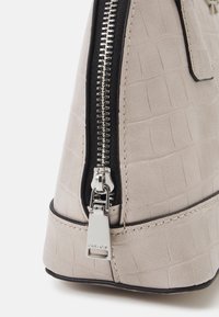 Ljus beige faux läderhandväska med ett präglat krokodilmönster, silverdragkedjestängning och svarta detaljer längs kanterna.