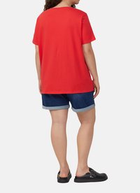 Czerwona bawełniana koszulka z krótkim rękawem, połączona z dżinsowymi szortami z podwiniętymi nogawkami. Czarne buty wsuwane dopełniają stylizację.