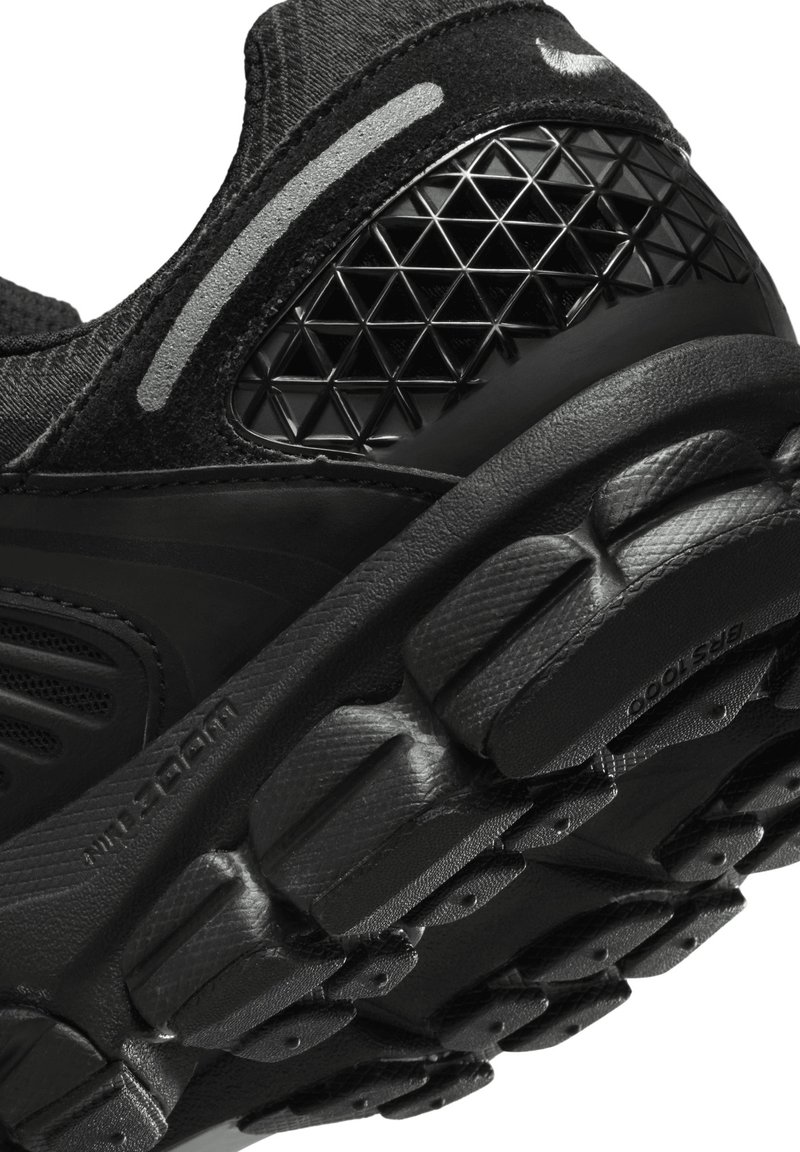 Chaussure de sport noire dotée d'un dessus en mesh texturé, d'une semelle en caoutchouc avec des motifs de traction définis, et d'accents géométriques sur le talon.
