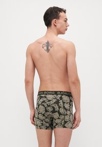 Shorts de boxe noirs et olives avec un motif de feuilles, ceinture élastique arborant le texte "BJÖRN BORG", présentant un design ajusté et une texture douce.