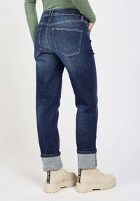 Dark blue denim jeans with a straight fit, featuring rolled cuffs, double back pockets, and a subtle textured pattern. Beige platform boots.