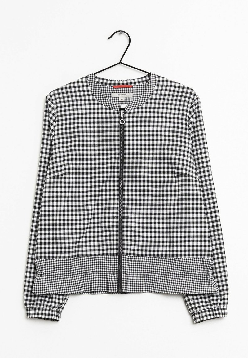 Chaqueta de cuadros en blanco y negro con mangas largas, cuello redondo, cremallera frontal y puños y dobladillo elásticos. Cuelga de un gancho negro.