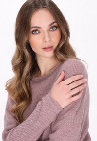 Stofzuig roze gebreide trui van textuurstof, met ronde halslijn en geribbelde manchetten. Het model staat met gekruiste armen en toont het gezellige ontwerp.