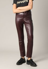 Bordeaux faux leren broek met een slim fit, hoge taille en glanzende afwerking. Gepaard met zwarte robuuste veterschoenen.