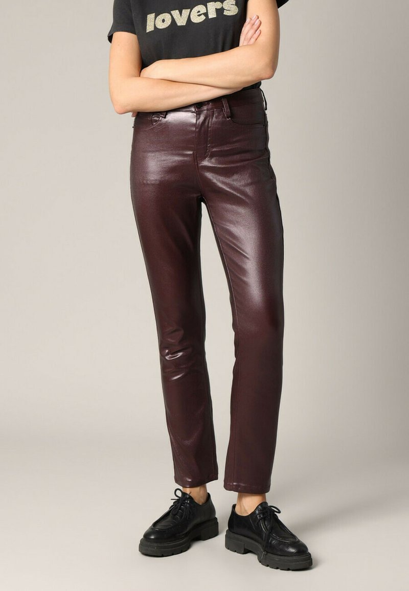 Bordeaux faux leren broek met een slim fit, hoge taille en glanzende afwerking. Gepaard met zwarte robuuste veterschoenen.