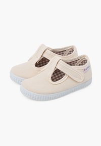 Scarpe in tela di un beige chiaro con una cinturino a T, suola in gomma bianca e fodera a quadrati marroni. Presenta un'etichetta sul lato.