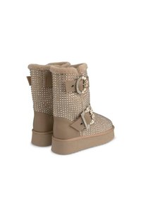 Beige laarzen met een zachte, met bont gevoerde binnenkant, versierd met zilveren studs en een met juwelen accentueerde gesp aan de zijkant. Platte rubberen zool, midden kuit hoogte.