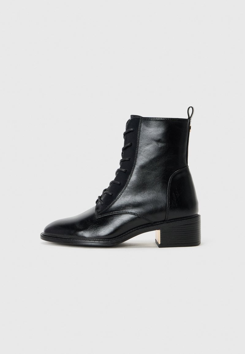 Bottine en cuir noir à lacets avec un talon bloc bas et une languette sur un fond gris clair uni.